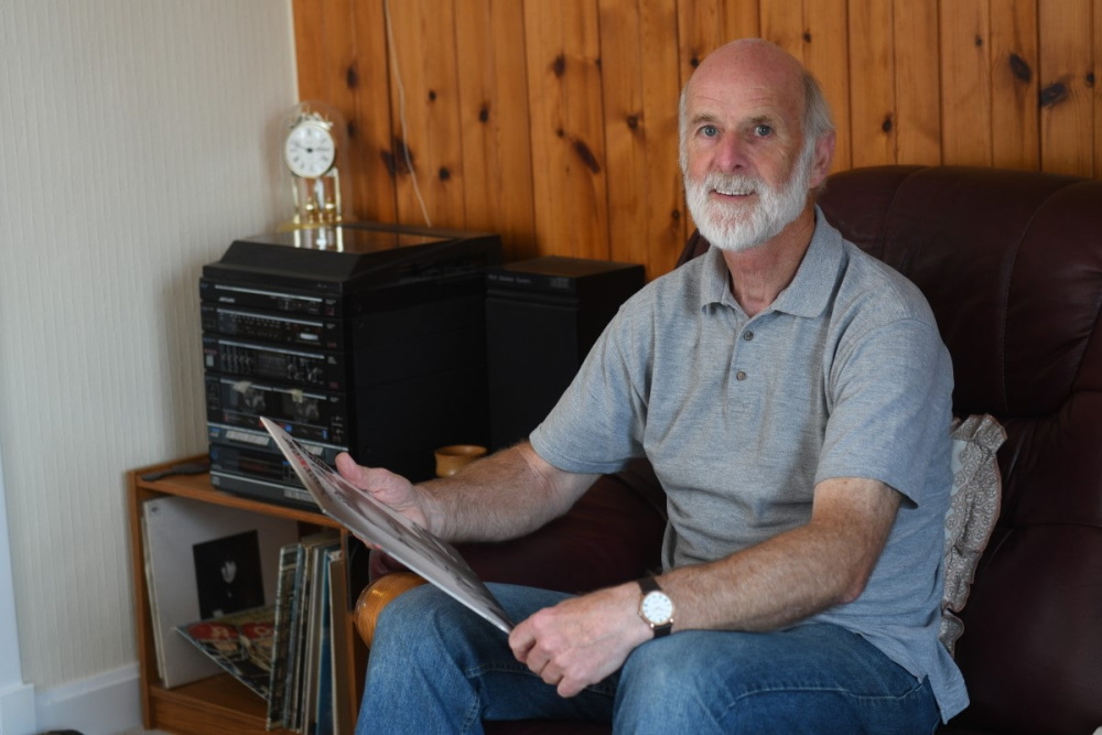 Man holding a record next to a record player. Leave a legacy gift in your will.