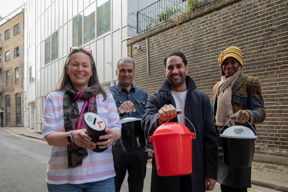 Four smiling Shelter volunteers hold collection tins and buckets