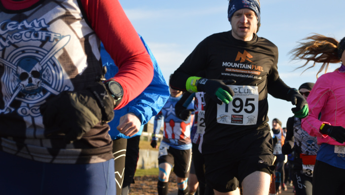 A man runs towards the camera, he has a race number on his t-shirt