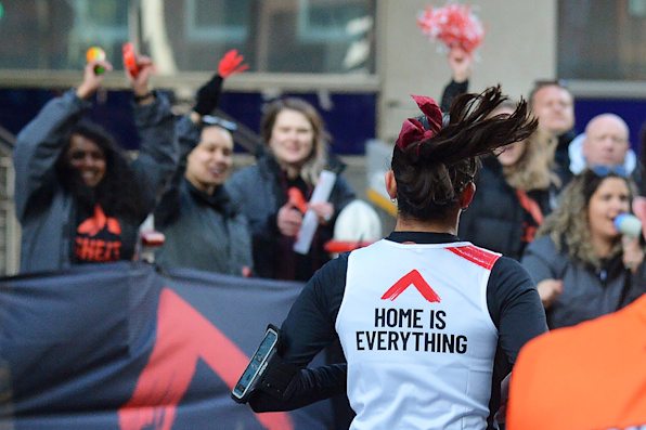 The back of a runner's head, they are waving to the crowd and are wearing a Shelter top that says Home is everything