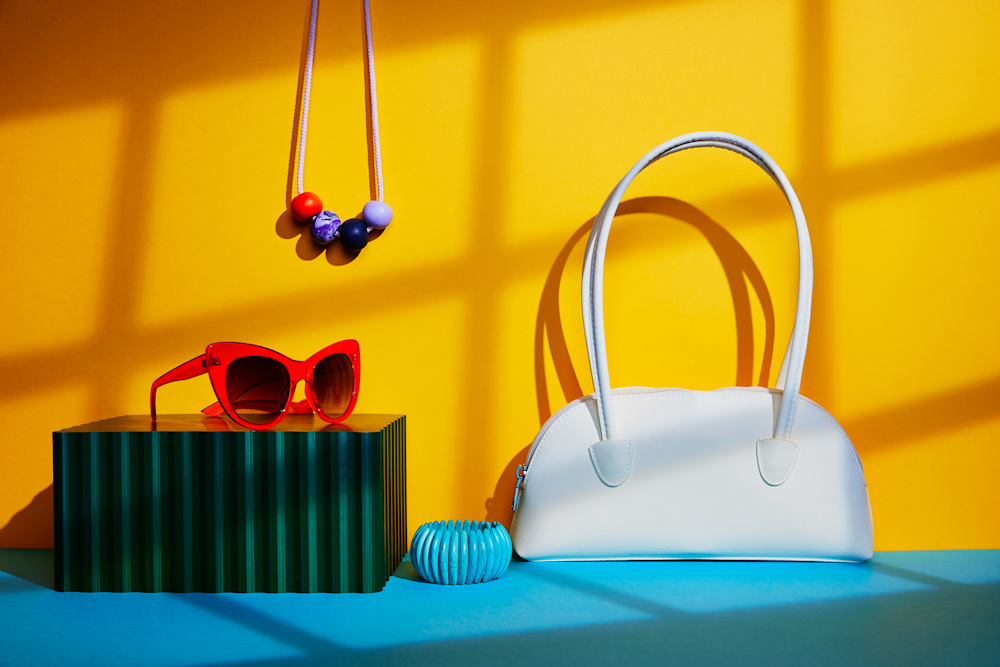 Red sunglasses with multi coloured beaded necklace, blue bracelet and white handbag