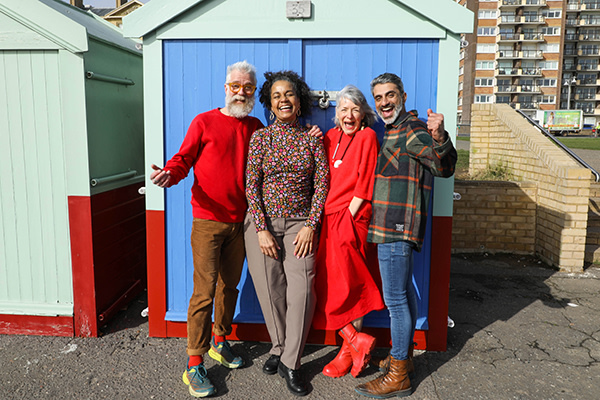 A group of four happy people standing in front of a shed during the day, each wearing an item of red