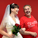 Someone in a wedding dress holding red roses and linking arms with someone in a Shelter Scotland top.