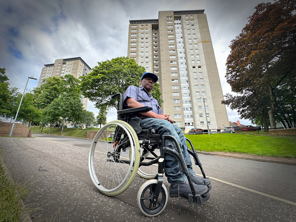 InnocentJakisa sits in his wheelchair in front of his multi-storey flat.