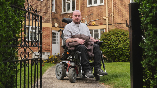 A defiant man sits in a wheelchair in the entrance to a block of flats