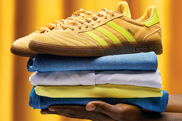 A hand holding a pile of neatly folded clothes with a pair of bright yellow sneakers on top