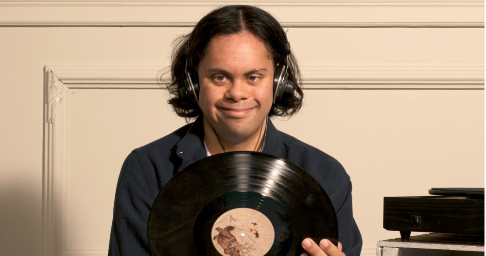 A young man wearing headphones smiles as he holds a vinyl record 
