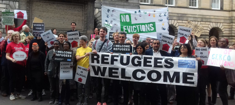 People pictured protesting with banners that say things like 'refugees welcome' and 'no evictions'.
