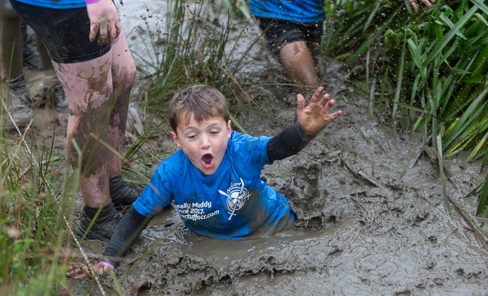 A child in a blue MacTuff t shirt wades through waist deep mud