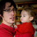 A parent pictured holding a child. Both are wearing red.