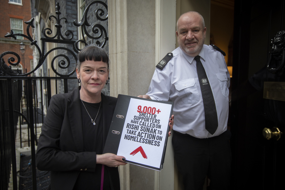 Shelter campaigner Amanda handing over a petition in a black folder to parliament saying '90,000 Shelter supporters have called on Rishi Sunak to take action on homelessness'. 