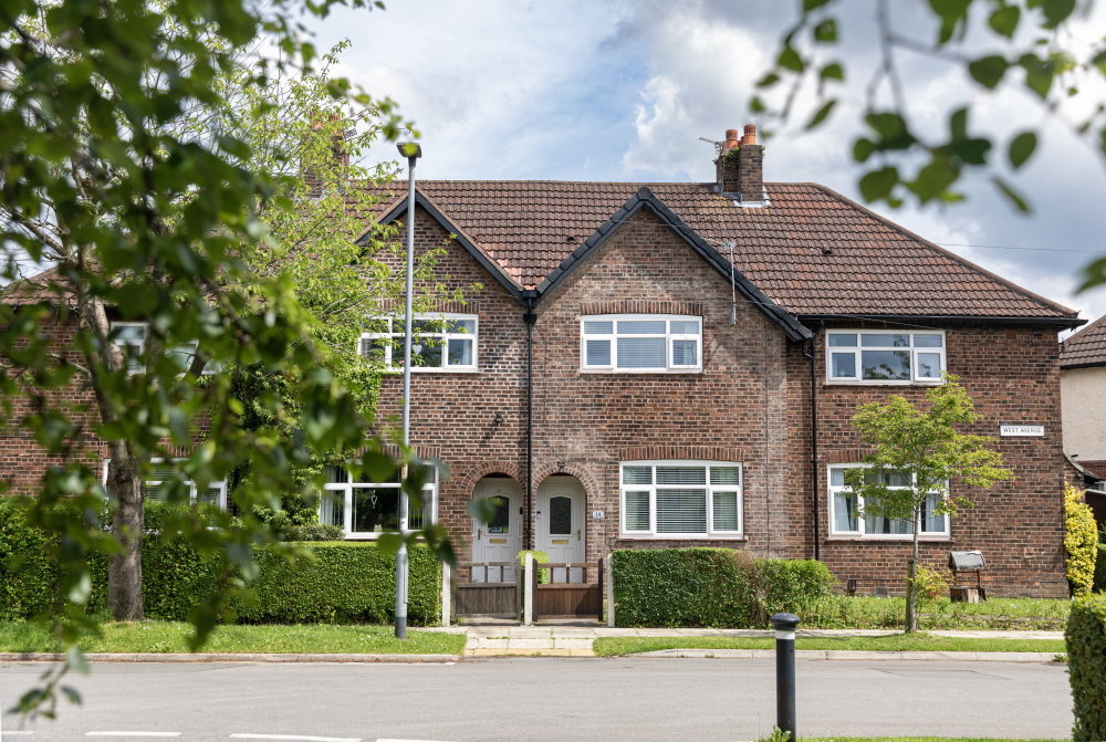 A semi-detached social home in Manchester with a green front lawn, trees and hedges.