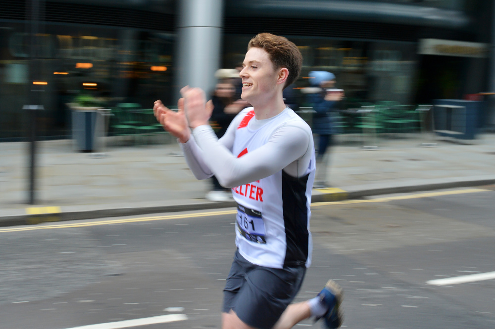A man wearing a Shelter vest runs past the cheer point at the London Landmarks Half Marathon, smiling and clapping.