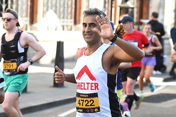 A man wearing a Shelter vest is running in a crowd and is giving a wave and a thumbs up.