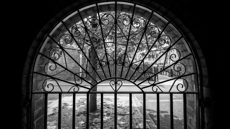 An ornate arched gate - visible on the other side is a housing complex surrounded by trees.