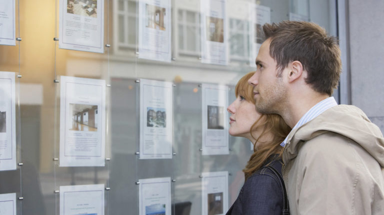 A couple looking at homes advertised in the window of a letting agency