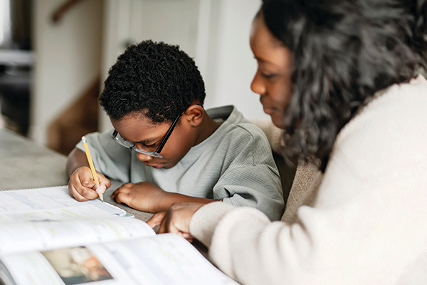 A mother helping her young son with his homework at a table. 