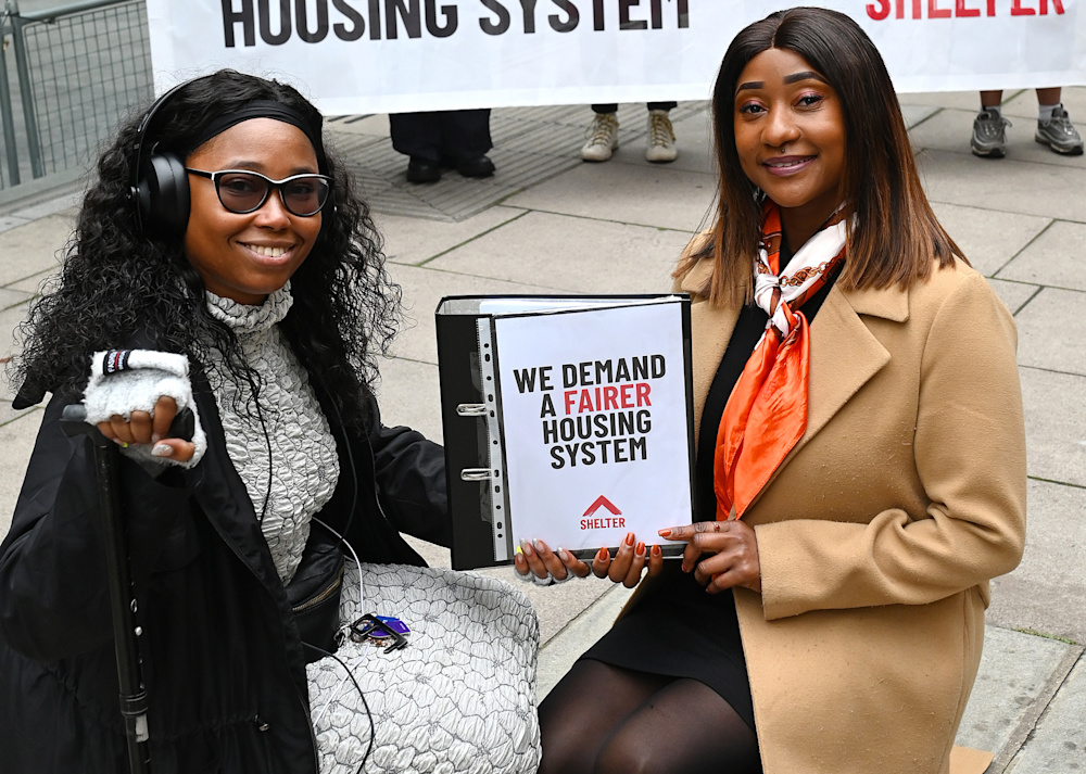 Two campaigners hold a file containing supporter signatures. The front of the file reads: 'we demand a fairer housing system'.