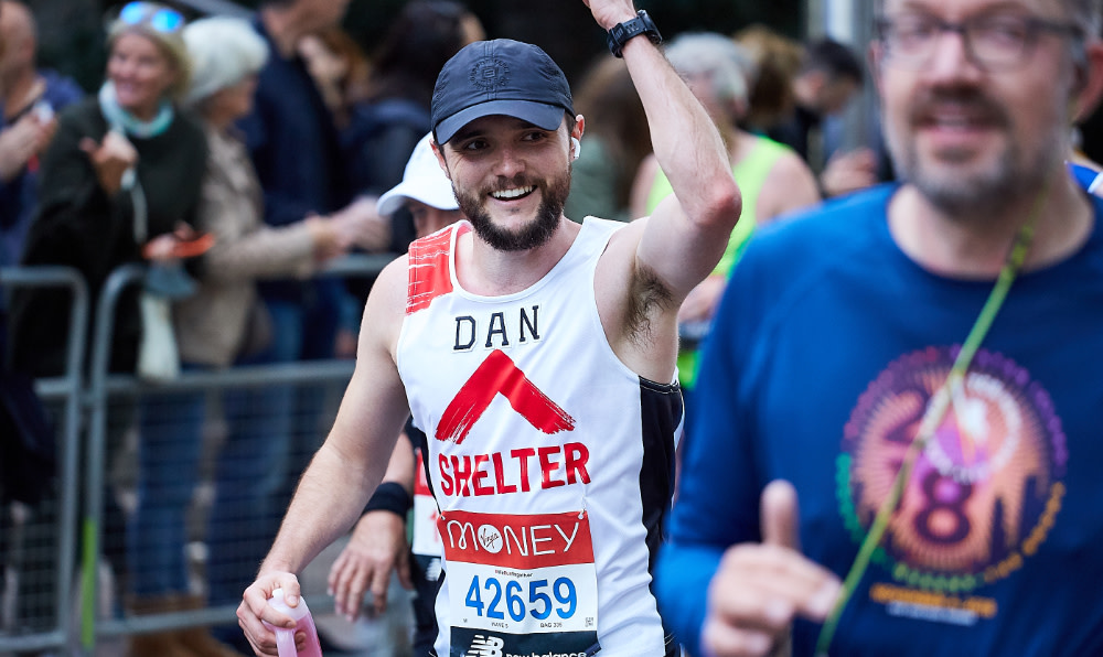 A runner in the Great North Run raising his hand and wearing a Shelter t-shirt
