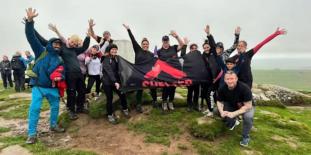 A group of hikers on Hadrian's Wall, waving and holding up a Shelter banner.