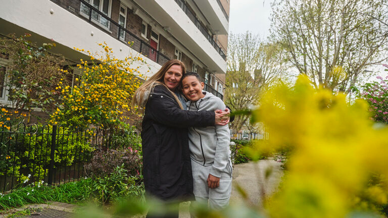 A mother hugs her son as she stands outside of their social home
