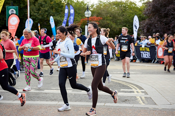 Two women in Shelter vests smile as they run past the cheer point of the Royal Parks Half Marathon.