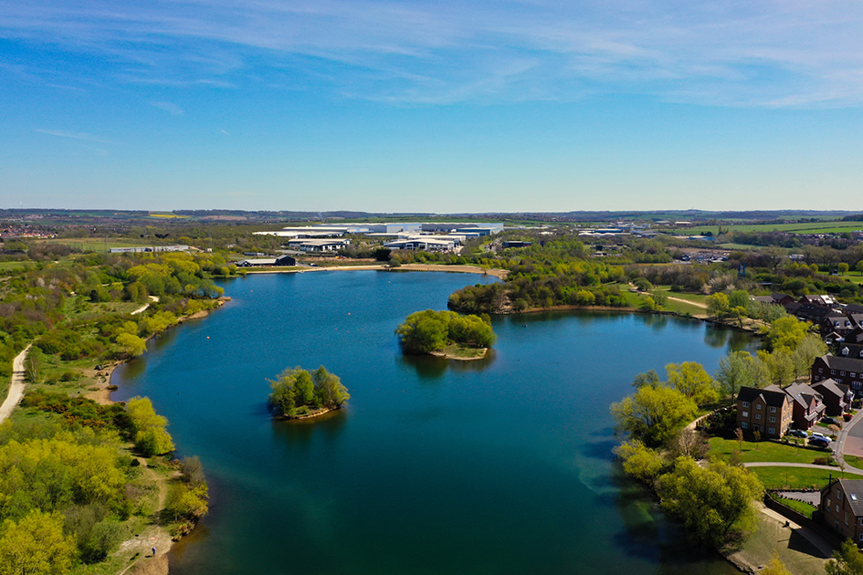 An aerial view of Manvers Lake, the venue for the Shiver for Shelter challenge. It's a beautiful deep blue and surrounded by trees.
