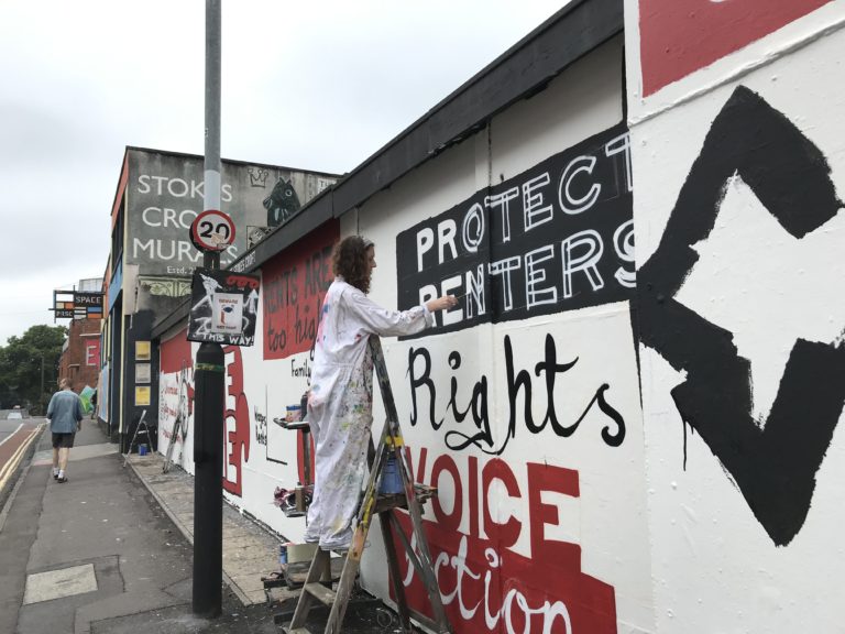 A Bristol campaigner painting a mural that reads 'Protect renters: rights, voice, action'