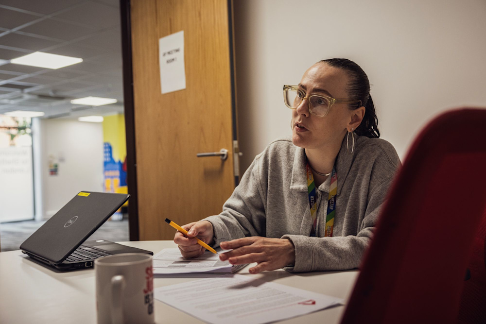 A woman wearing a Shelter lanyard is sitting in an office and filling in paperwork.