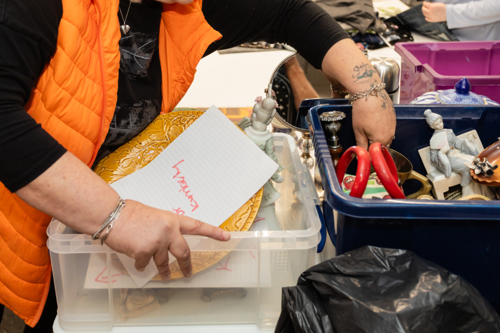 A Shelter furniture shop volunteer sorts through two plastic boxes containing various ornaments and bric-a-brac.