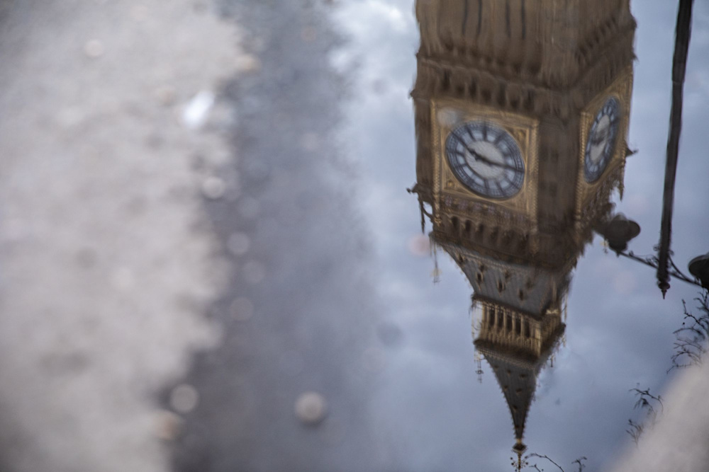 The clock face of Big Ben reflected in a puddle of water on a rainy day in Westminster.