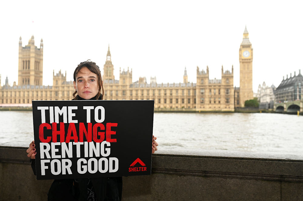 A Shelter campaigner holds a sign that reads 'Time to change renting for good'. The Houses of Parliament are in the background.