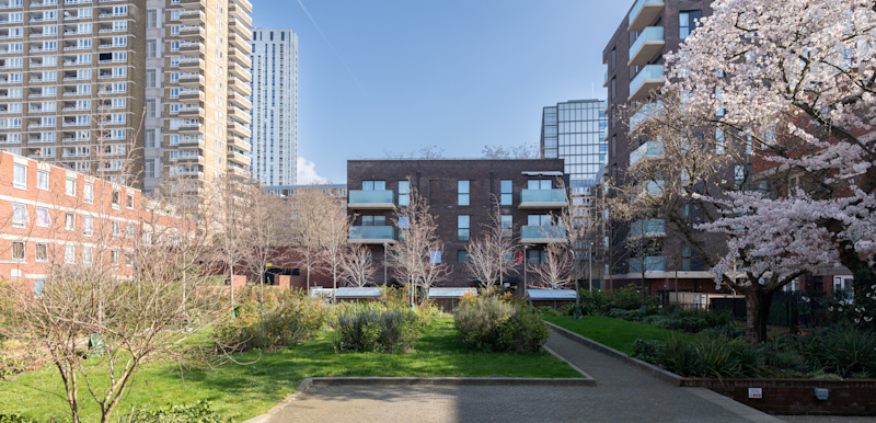 A green space with social housing flats surrounding it and trees in blossom