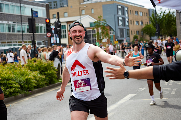 A runner wearing a Shelter vest passes the cheer point. He reaches out his hand to give one of the Shelter cheerers a high five.