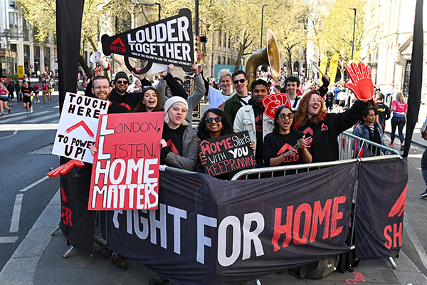A team of Shelter volunteers standing at a cheer point. They are smiling and are holding placards with a 'Fight for home' banner.