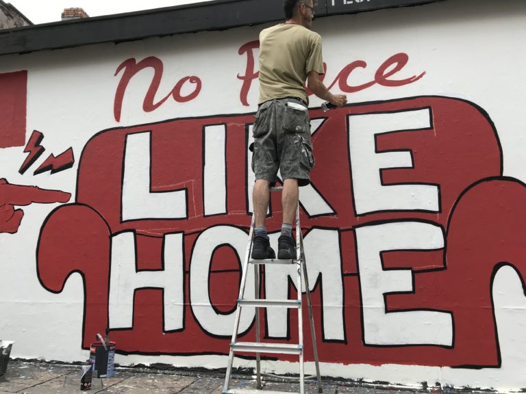 A Bristol campaigner painting a mural that reads 'No place like home' with an illustration of a red sofa.