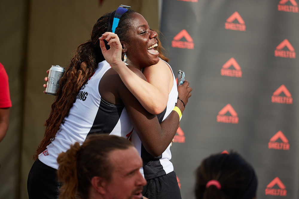 Two women wearing Shelter vests hug in celebration after finishing their race.