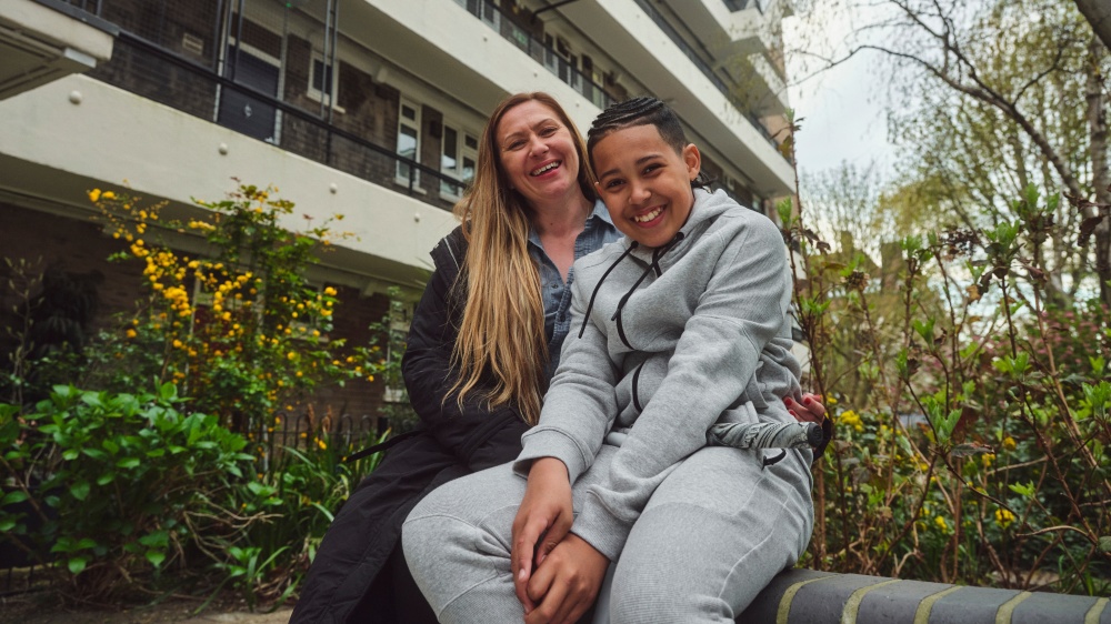 Angela and son Cardi sit together in a garden outside a flat block