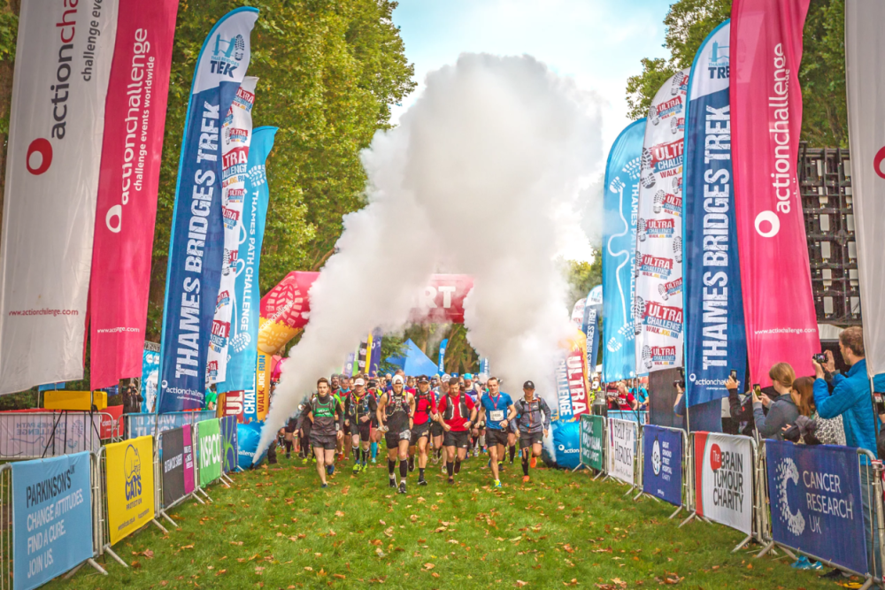Runners set off from the start line, passing under jets from a smoke machine. On either side of them are banners for Ultra Challenge and different charities.