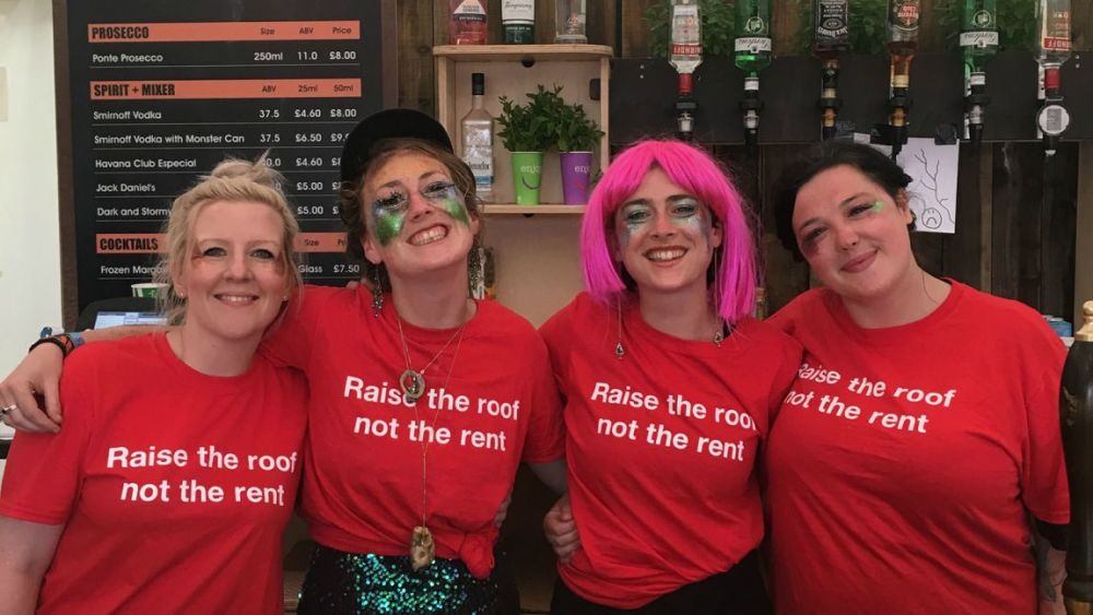 Four Shelter bar staff volunteers at a music festival wearing Shelter t-shirts and sparkly festival make up
