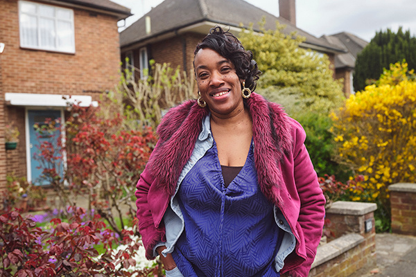 Sarah stands smiling in front of a house