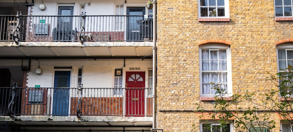 Two floors of social housing flats, with balconies and colourful red and blue front doors.