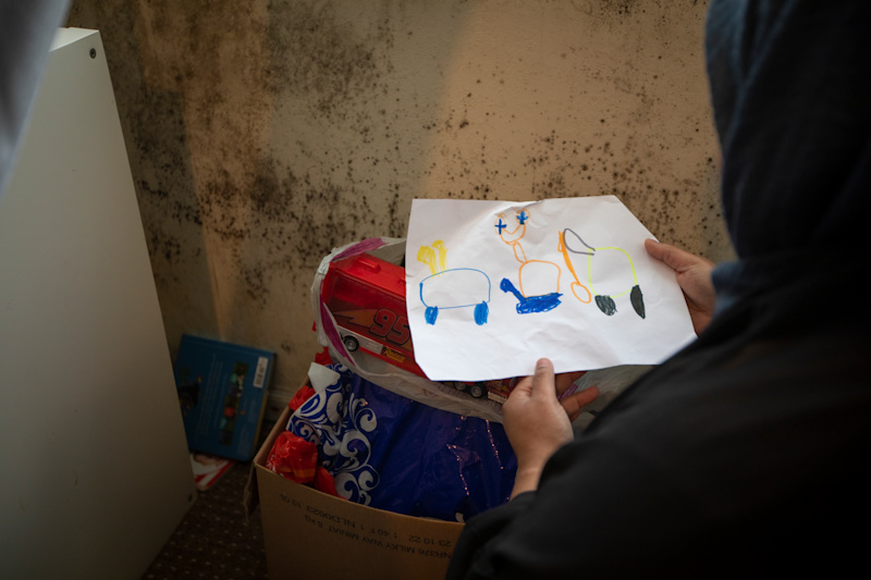 A person holds up an image of a drawing in a room which has heavy mould on the wall 