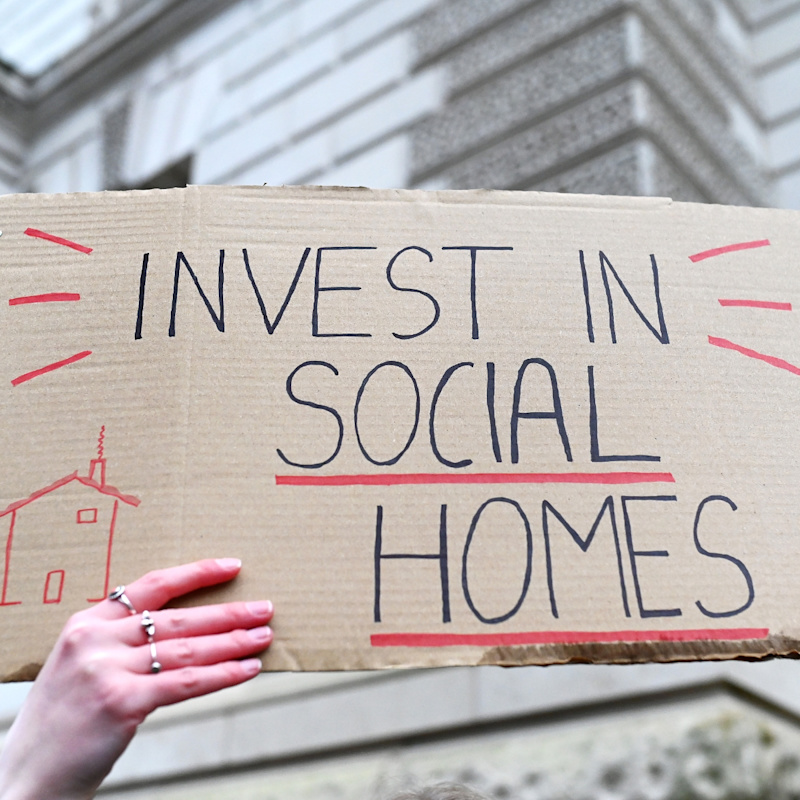 A cardboard protest sign with the message 'invest in social homes' written in black and red ink.