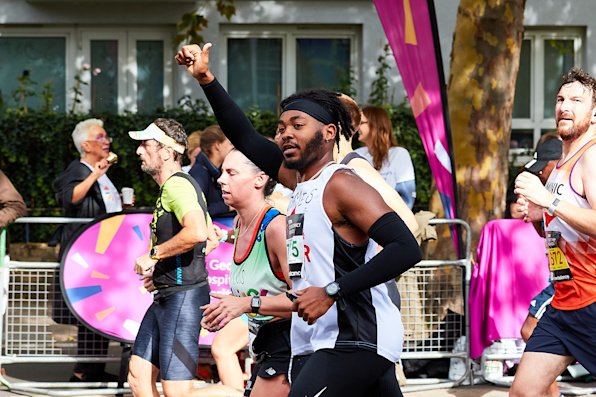 A Black man running in a shelter vest with thumbs up