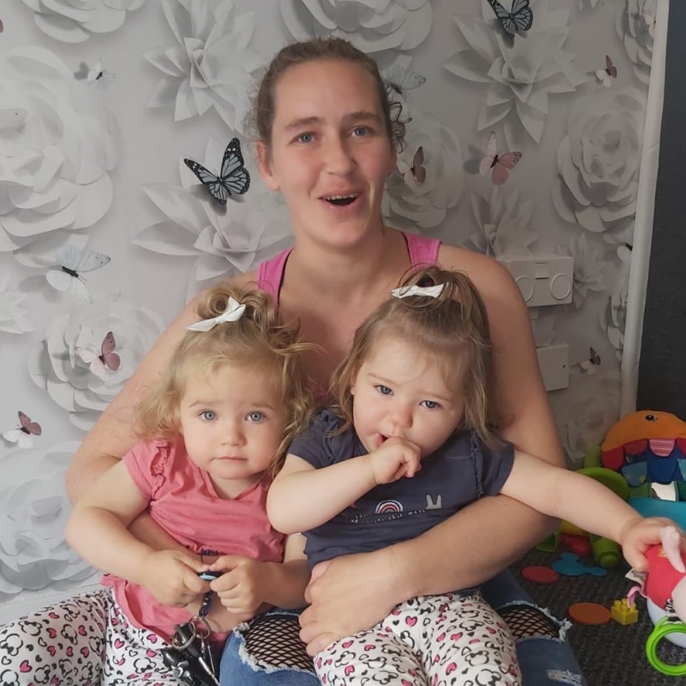 CJ and her two young girls, in their home. They look happy.
