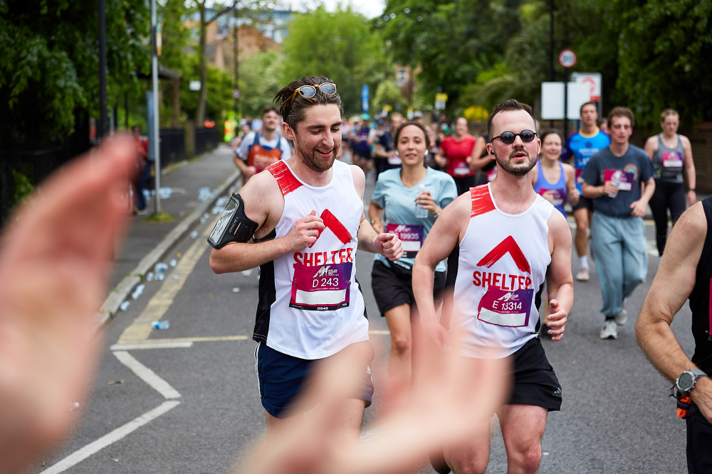 Two men in Shelter vests run past the cheer point - a supporter's clapping hands are in the foreground