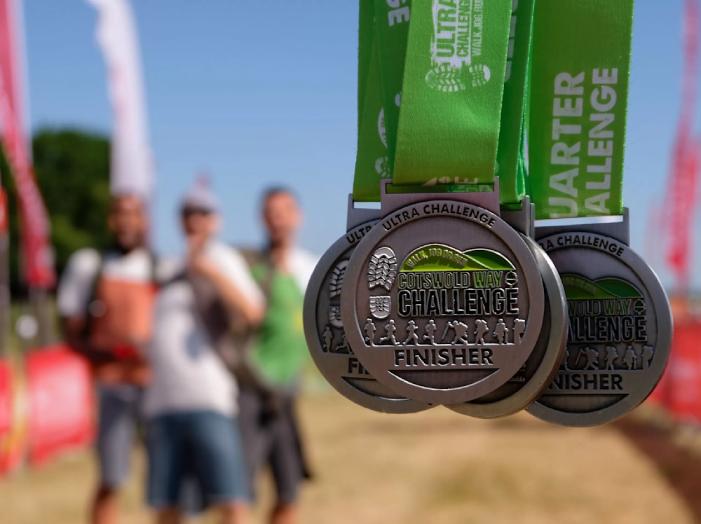 Close up of a handful of Cotswold Way Ultra Challenge finisher medals on green ribbon.