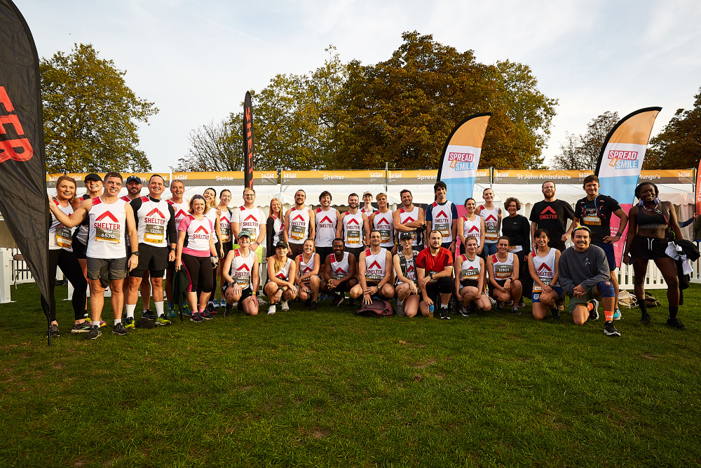 A big group of runners wearing Shelter vests and posing for a photo before their race, next to a Shelter banner.