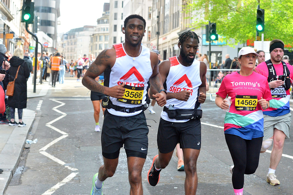 Two men running together in Shelter vests pass the cheer point of their race.